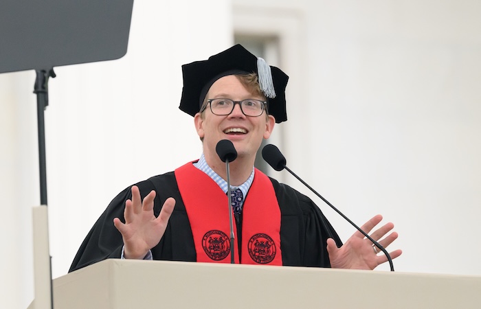 Image of Hank Green speaking at a podium. He is wearing black and red regalia.