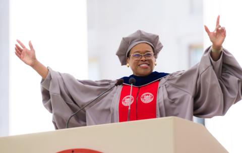 Image of Chancellor Melissa Nobles speaking at the podium, she is smiling and both her hands are raised