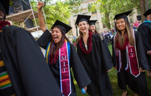 Image of undergraduates in line to receive their diplomas, one female graduate has her hand up