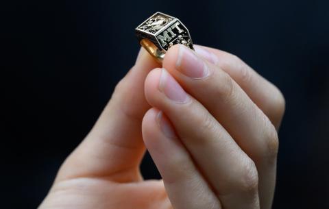 Image of a graduate's hand holding the Class of 2025's brass rat ring