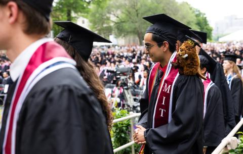 Image of graduates lined up to receive their diploma. One of the graduates has a stuffed beaver animal on his shoulder.