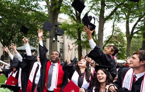 Image of the graduates in the audience smiling and throwing their caps in the air