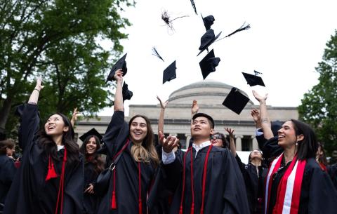 Image of the graduates throwing their caps in the air in front of Killian Court
